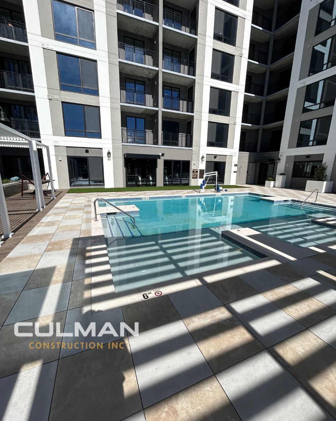 Pool area with light colored stone and a modern building, COLMAN CONSTRUCTION INC. is branded at the bottom left.