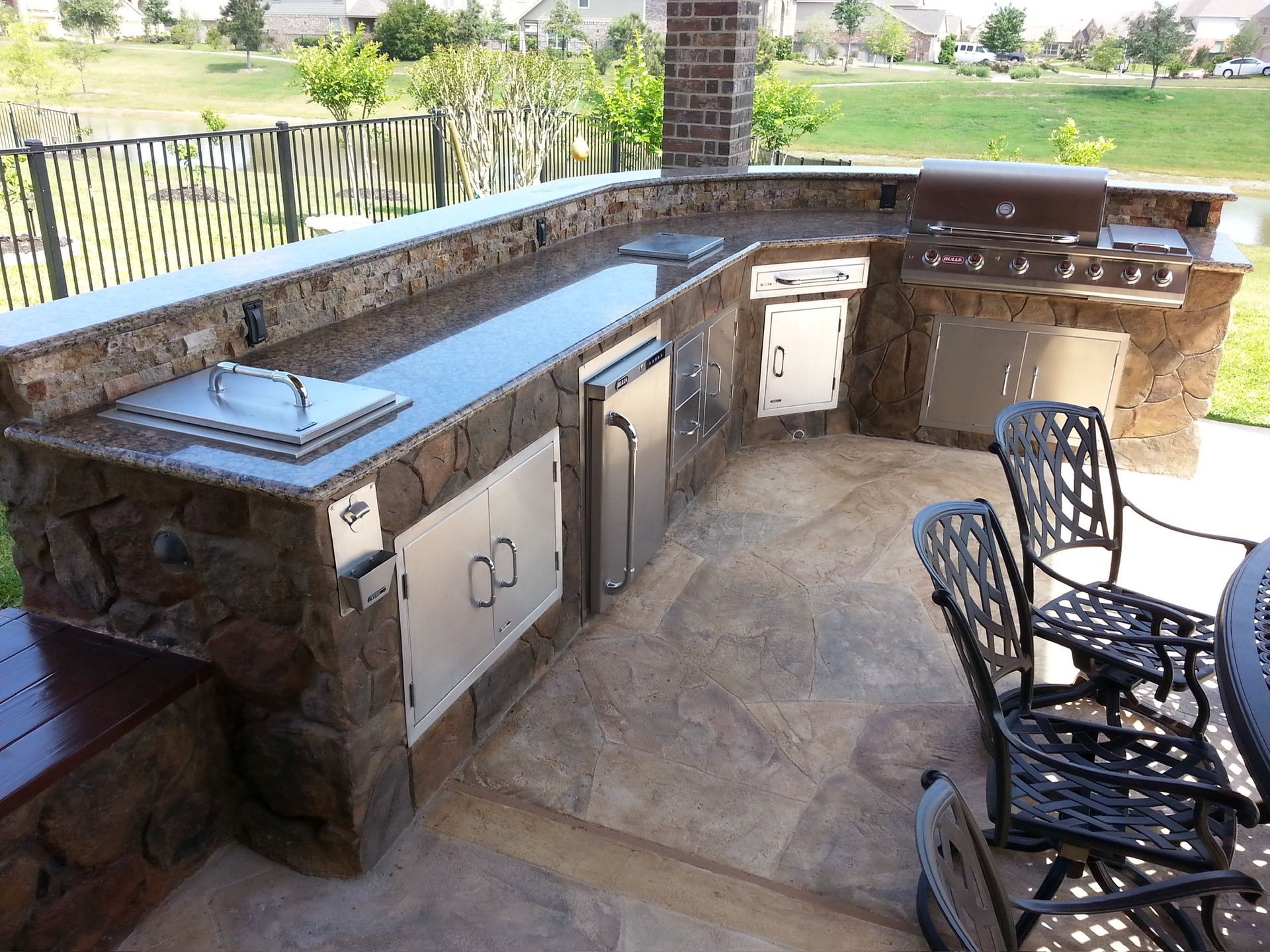 Outdoor stone kitchen with built-in grill, sink, and cabinets on a covered patio