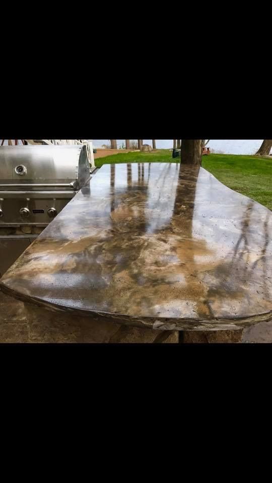 Wet, reflective stone or concrete tabletop outdoors beside a stainless steel grill.