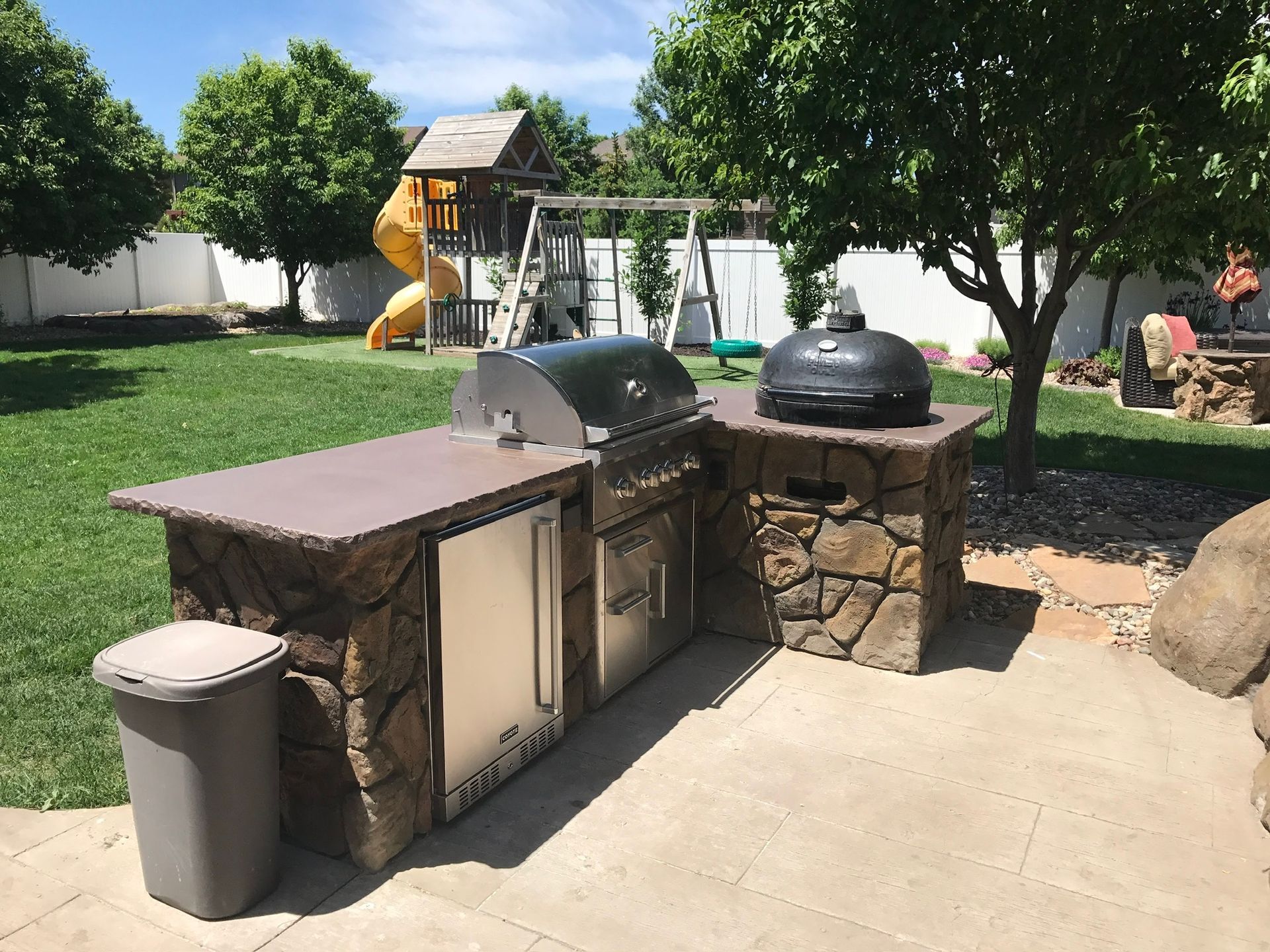 Backyard outdoor grill station with stone counters, covered grill, and patio seating area