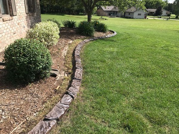 Curved stone border edging a lawn beside a brick house and shrubs