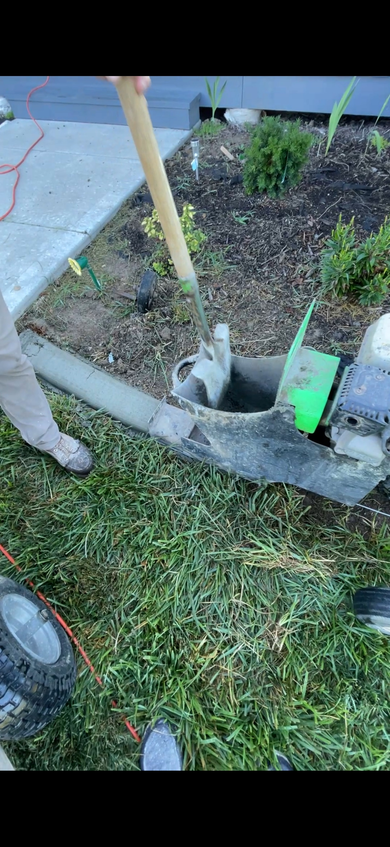 Garden tools beside a small plant bed with a shovel, broom, and a green tag near the curb