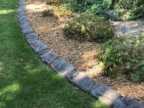 Curved stone border edging a landscaped garden bed beside a green lawn.