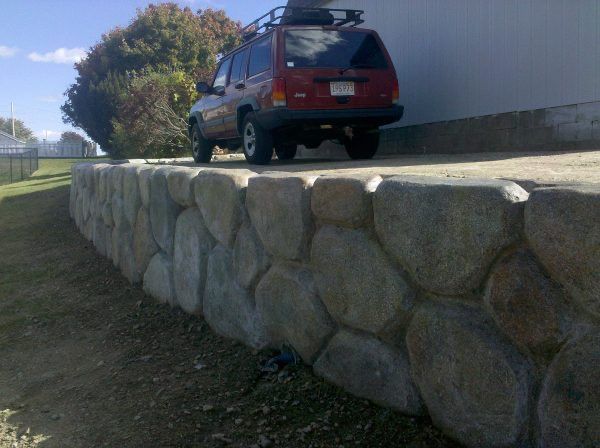 Red SUV parked atop a stone retaining wall beside a white building