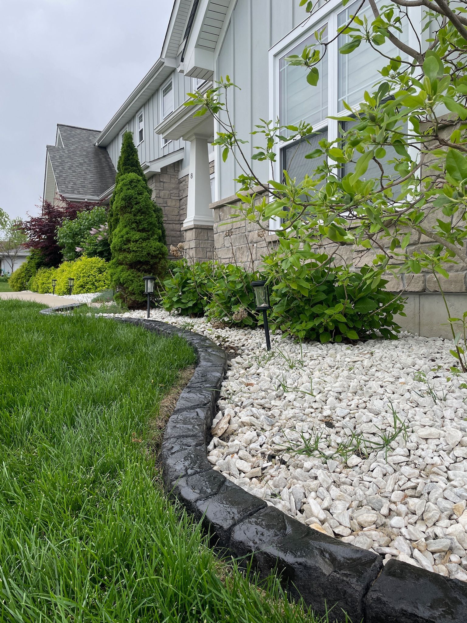 Landscaped front yard with green lawn, white stones, and a stone-lined garden bed beside a house.