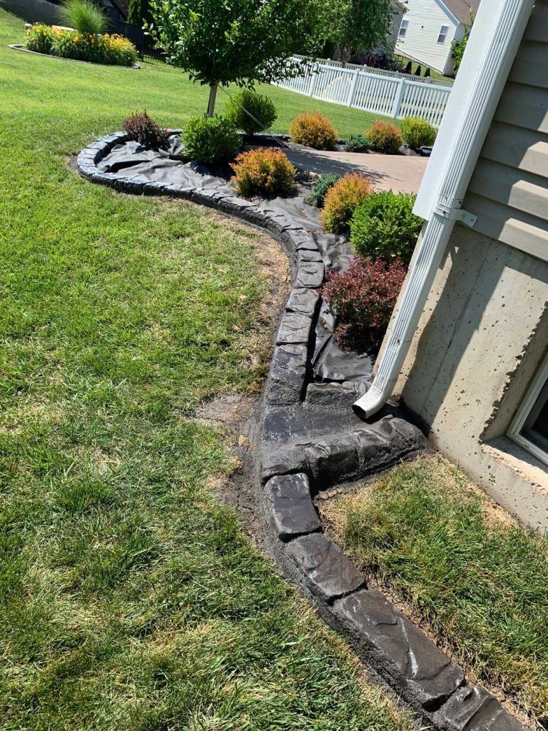 Curved brick landscape edging beside a house with mulch beds and trimmed shrubs over green lawn