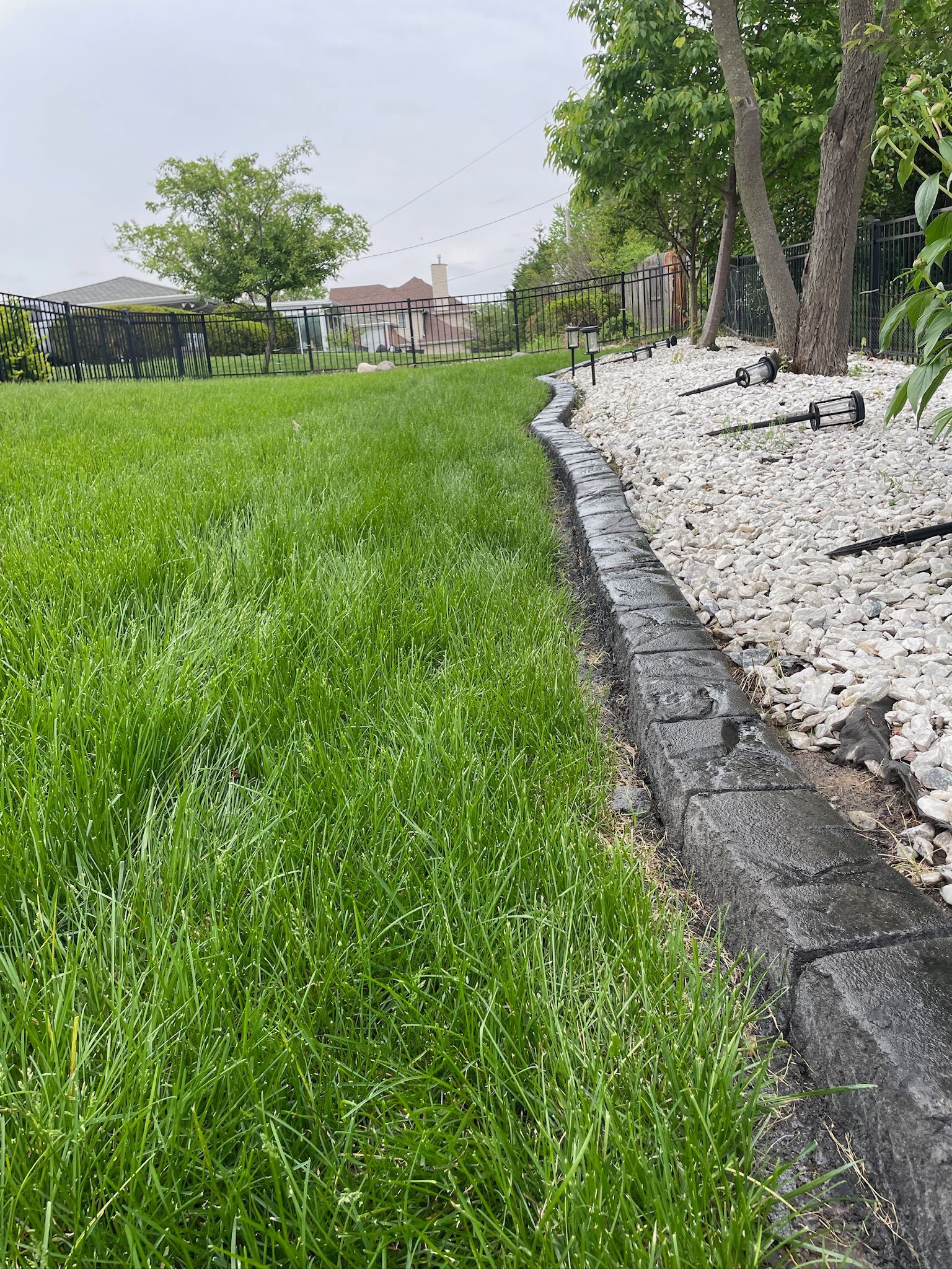 Grassy park lawn beside a stone border and trees on a cloudy day