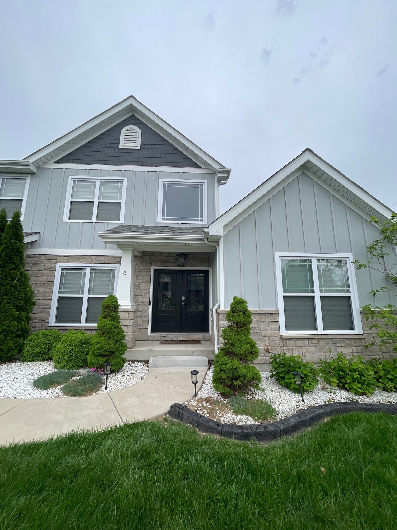 Gray two-story house with black front door, white trim, and a green lawn and walkway.
