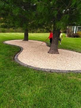 Person in red stands by a tree in a curved gravel garden path surrounded by green grass