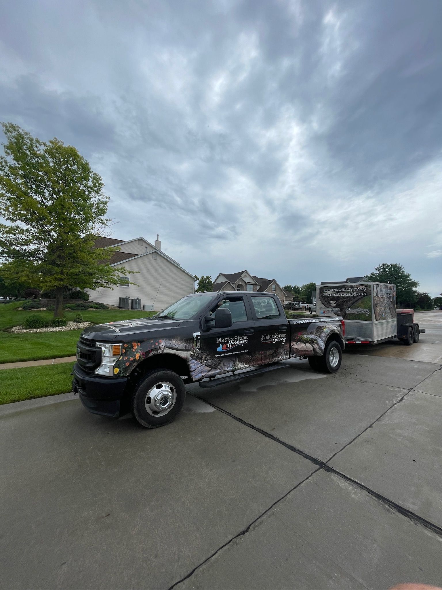Black pickup truck towing a trailer on a suburban street under cloudy skies