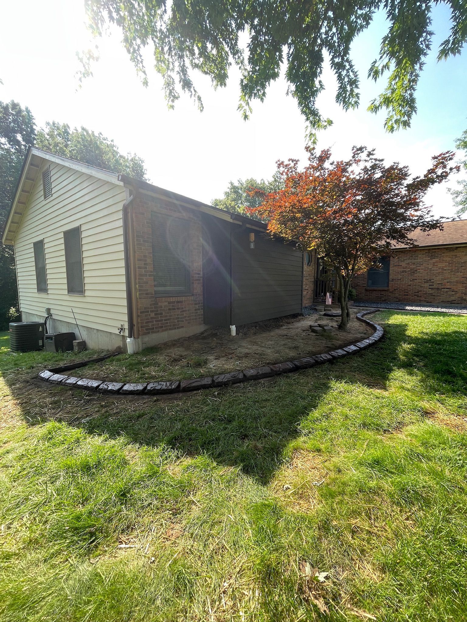 Small stone house with a screened porch, surrounded by a grassy yard and trees in bright sunlight.