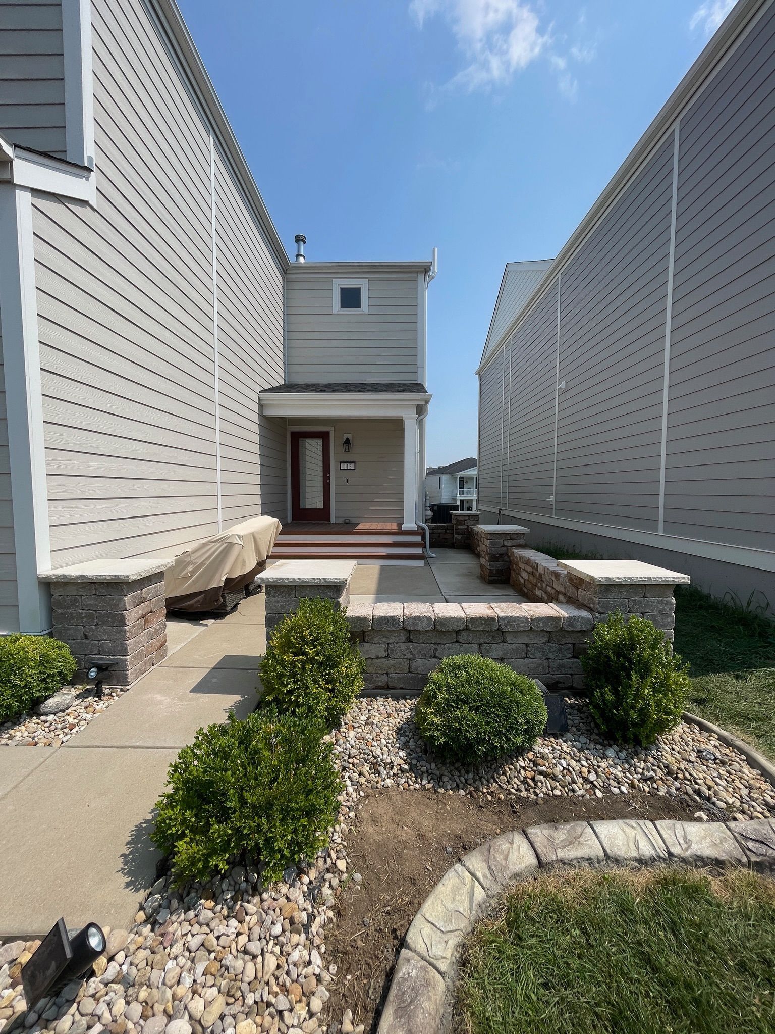 Modern house entry path with white siding, stone steps, and landscaped shrubs between tall side walls