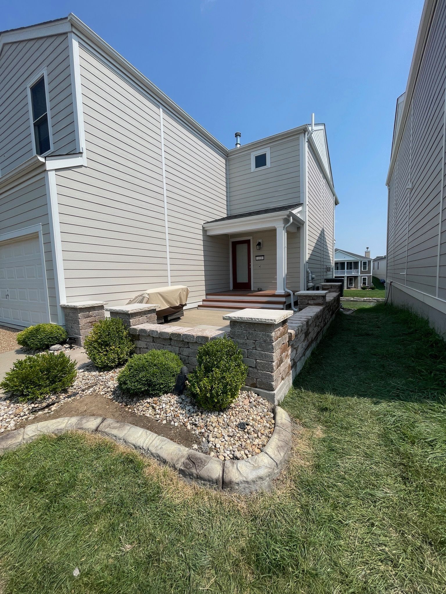 Modern beige townhouse with small landscaped front yard and stone planter under a clear blue sky