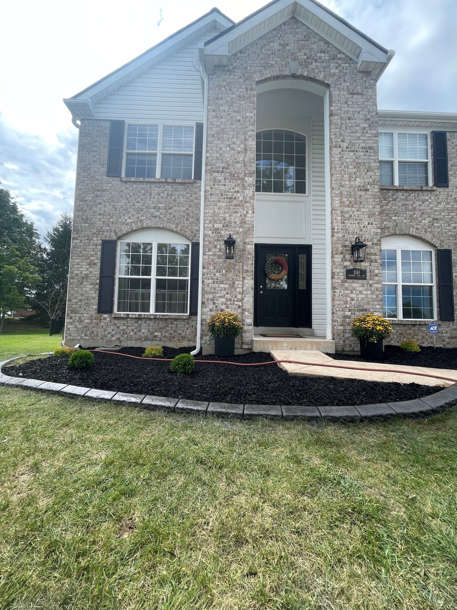 Two-story brick house with central arched entry, black shutters, and landscaped front lawn