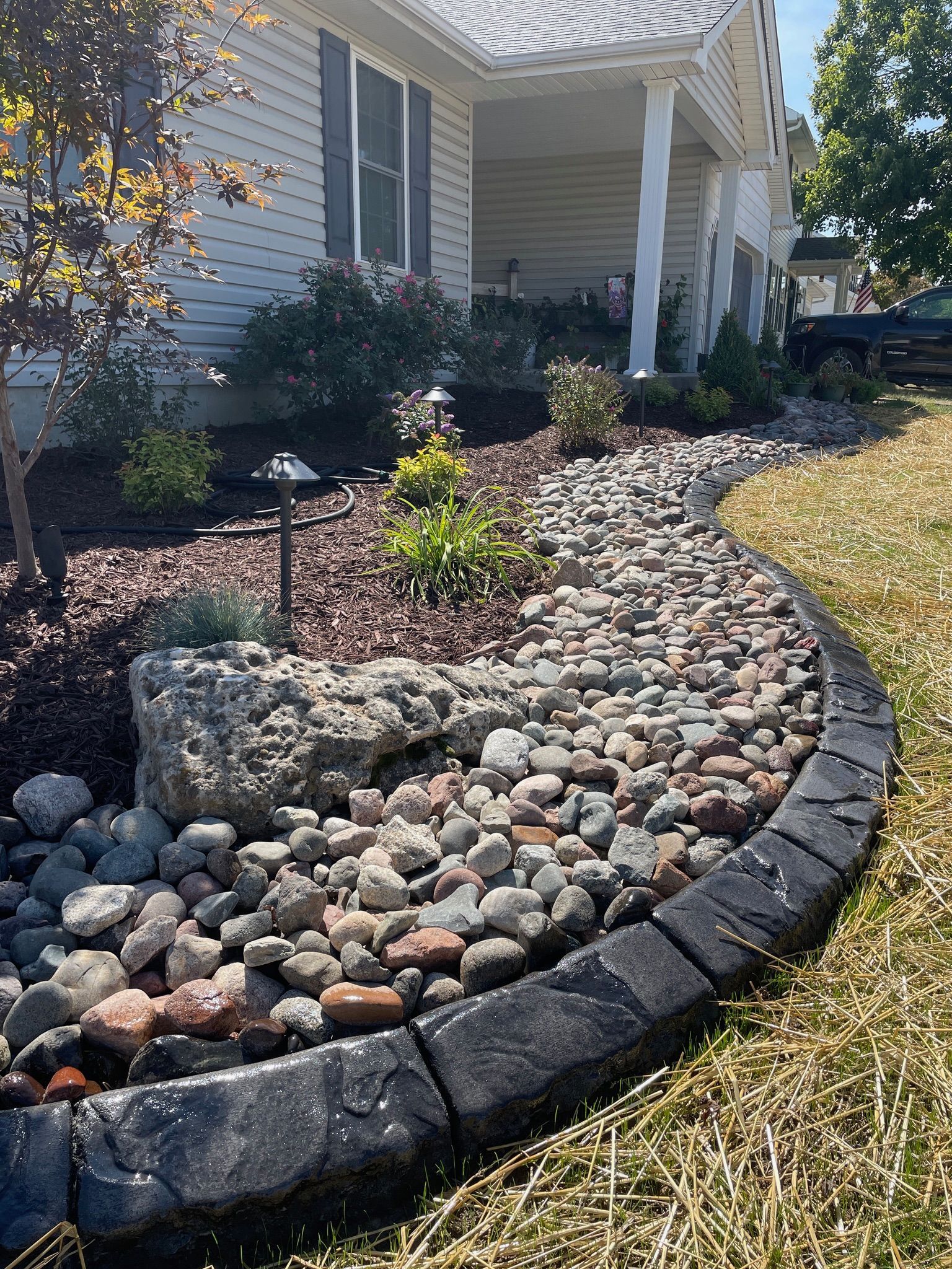 Front yard rock garden with curved stone border and a house porch in the background