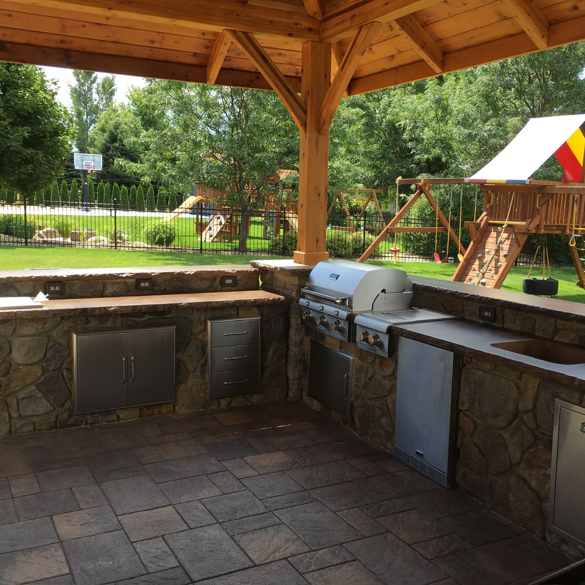 Covered outdoor grill station with stone counters and stainless steel grills in a park pavilion