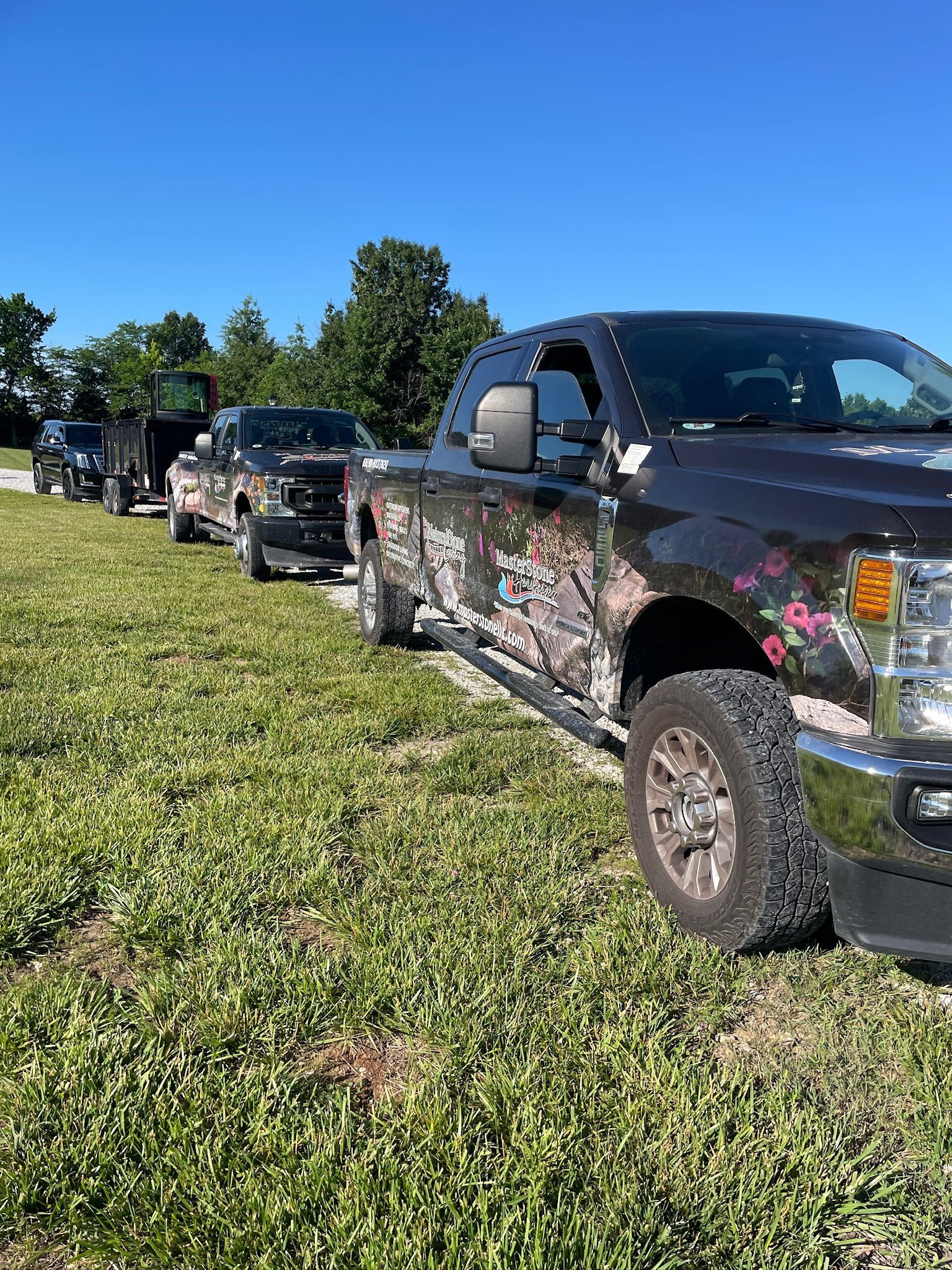Camouflage pickup trucks parked in a grassy field under a clear blue sky