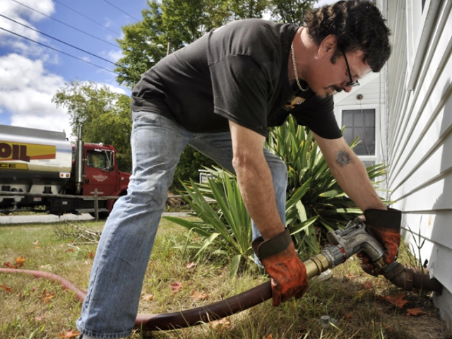 A man is pumping gas into a house with an oil truck in the background