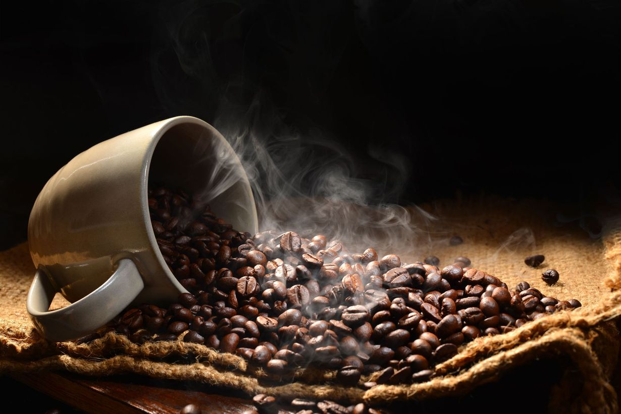 A cup of coffee is being poured into a pile of coffee beans.