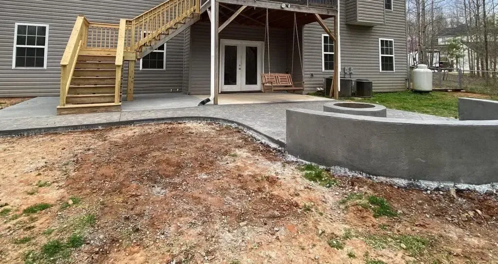 Backyard with concrete patio, stairs to a deck, and retaining wall.