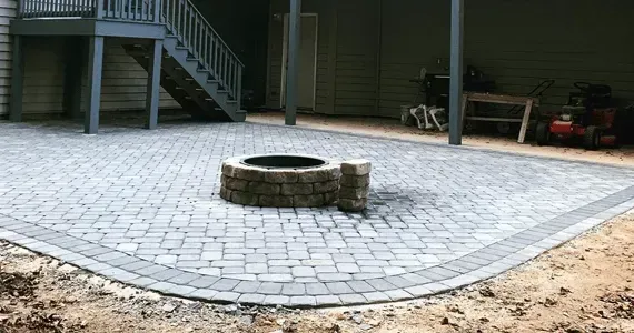 Stone paver patio with fire pit under a deck.