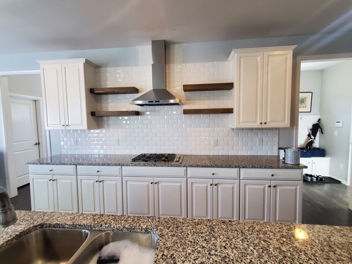 Kitchen with white cabinets, tile backsplash, stainless hood, and granite countertops.