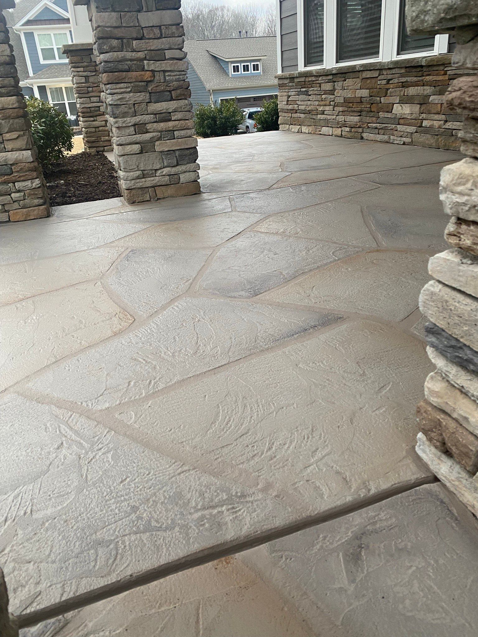Stone patio with gray concrete flooring, surrounded by stone columns and house facade.