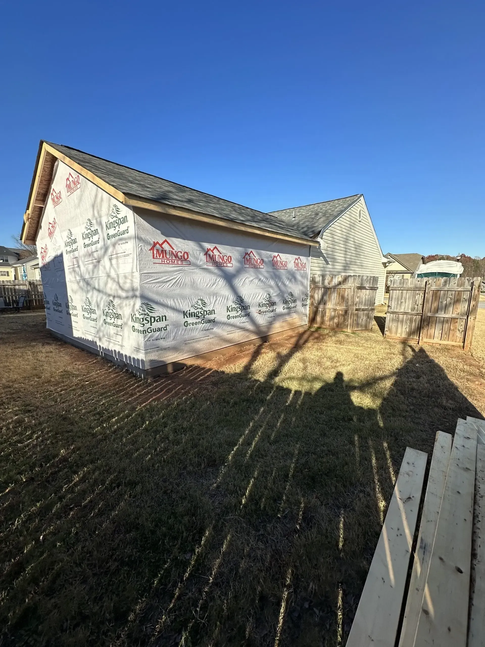 A partially built shed covered in protective wrap on a sunny day.