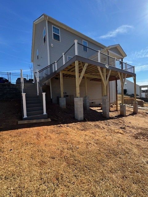 A two-story house with a wooden deck and stairs. The deck has white railings and is supported by concrete pillars.