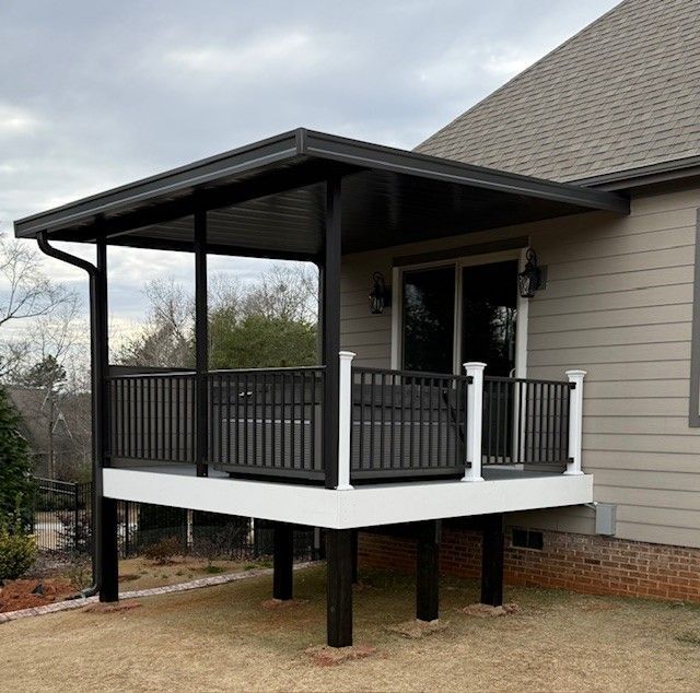 Black and white deck with overhead roof, railing, and columns extending from the house.