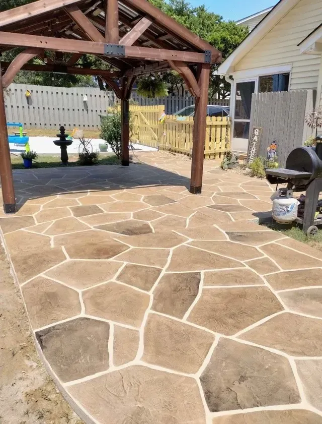 Brown flagstone patio with wooden pergola, near a yellow house. A black grill and propane tank are visible.