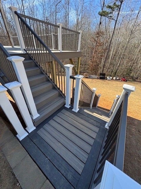 Composite deck with stairs and railings. Gray decking and dark gray and white railings in a backyard setting.
