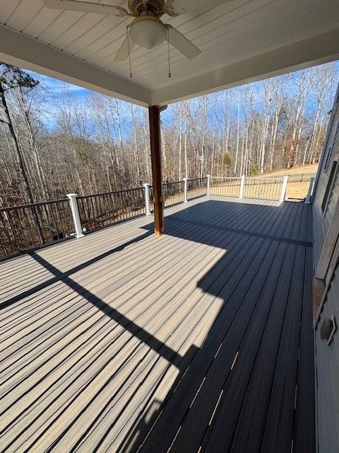 Covered deck with gray composite decking, brown posts and railing, overlooking a wooded area on a sunny day.