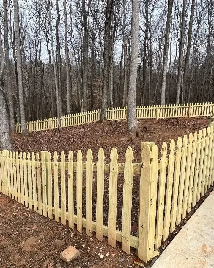 Yellow picket fence in wooded area, framing a sloped yard.