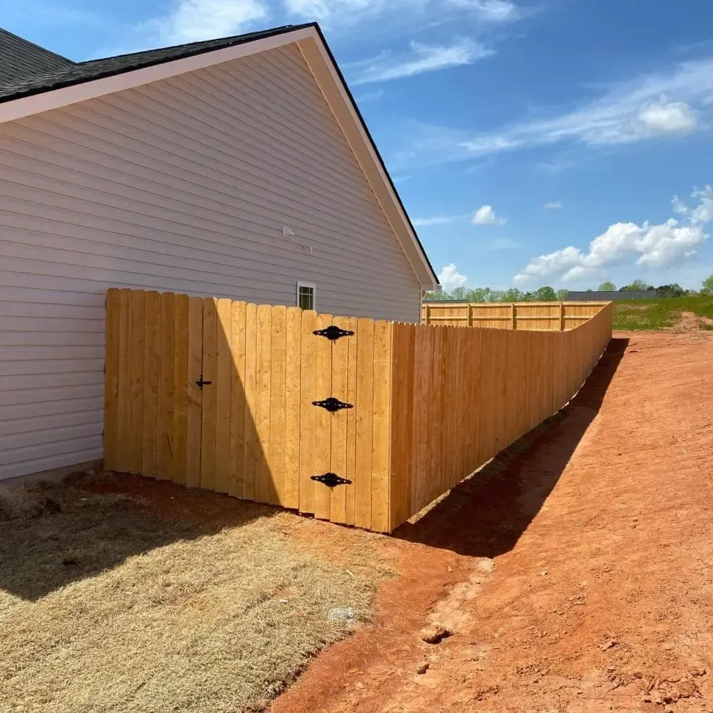 Wooden fence attached to a light-colored house with a blue sky background.