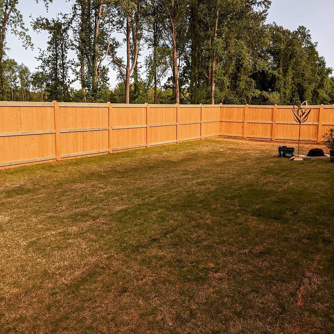 Wooden fence surrounds a grassy backyard, with trees in the background.