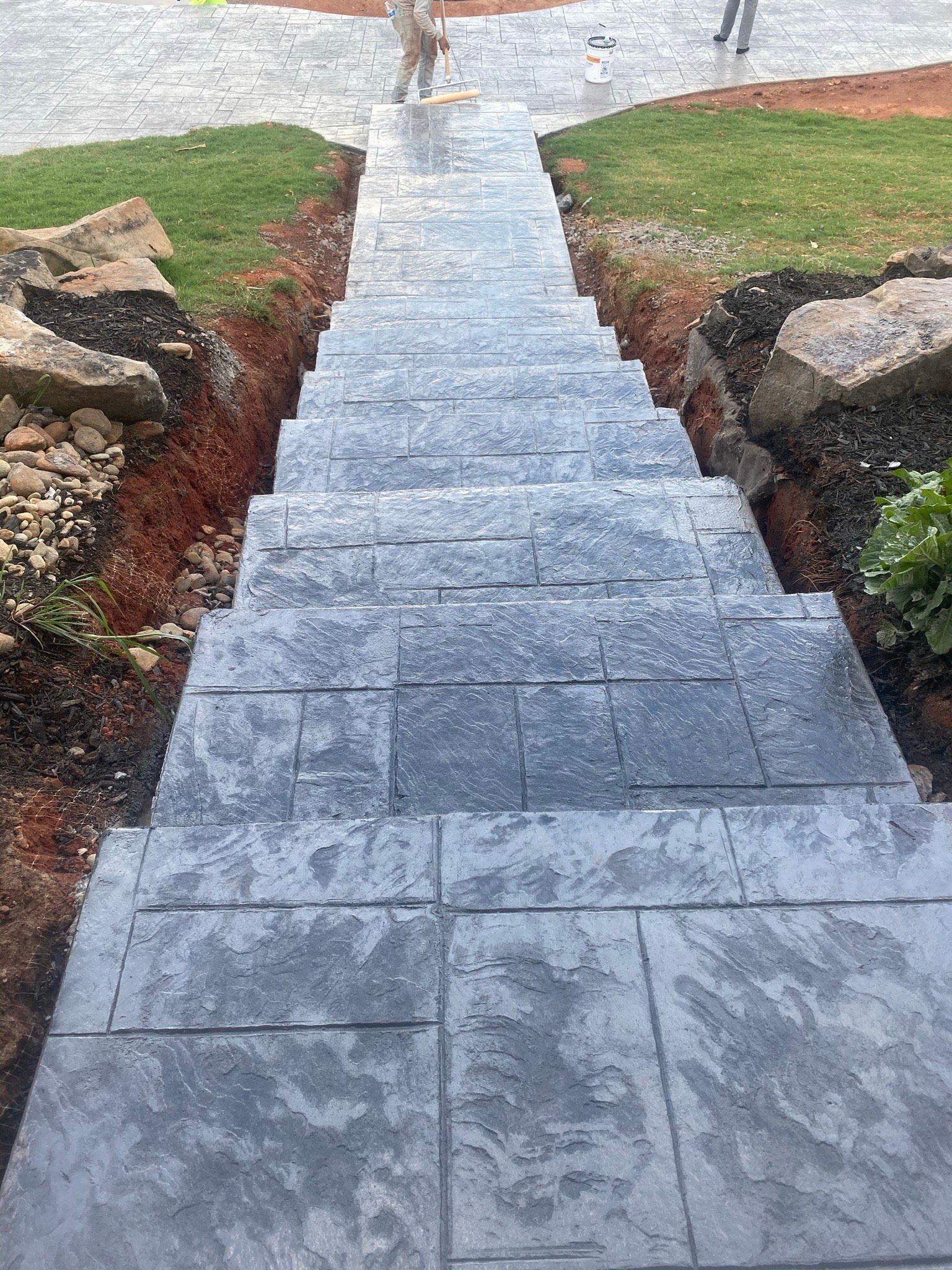 Stone steps leading down, flanked by exposed earth and grass, with two people in the background.