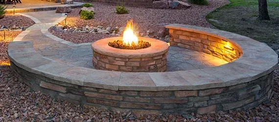 Fire pit with a stone surround and built-in bench, with a pathway and garden in the background.