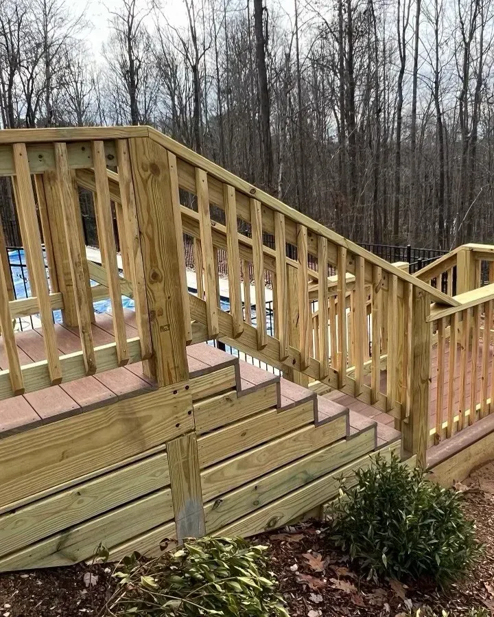 Wooden deck with stairs and railings, surrounded by trees.