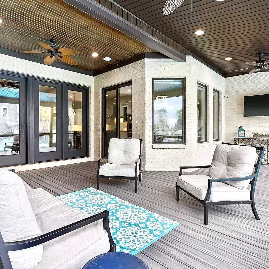 Outdoor patio with seating, light gray cushions, blue rug, brick walls, dark trim, and a TV.