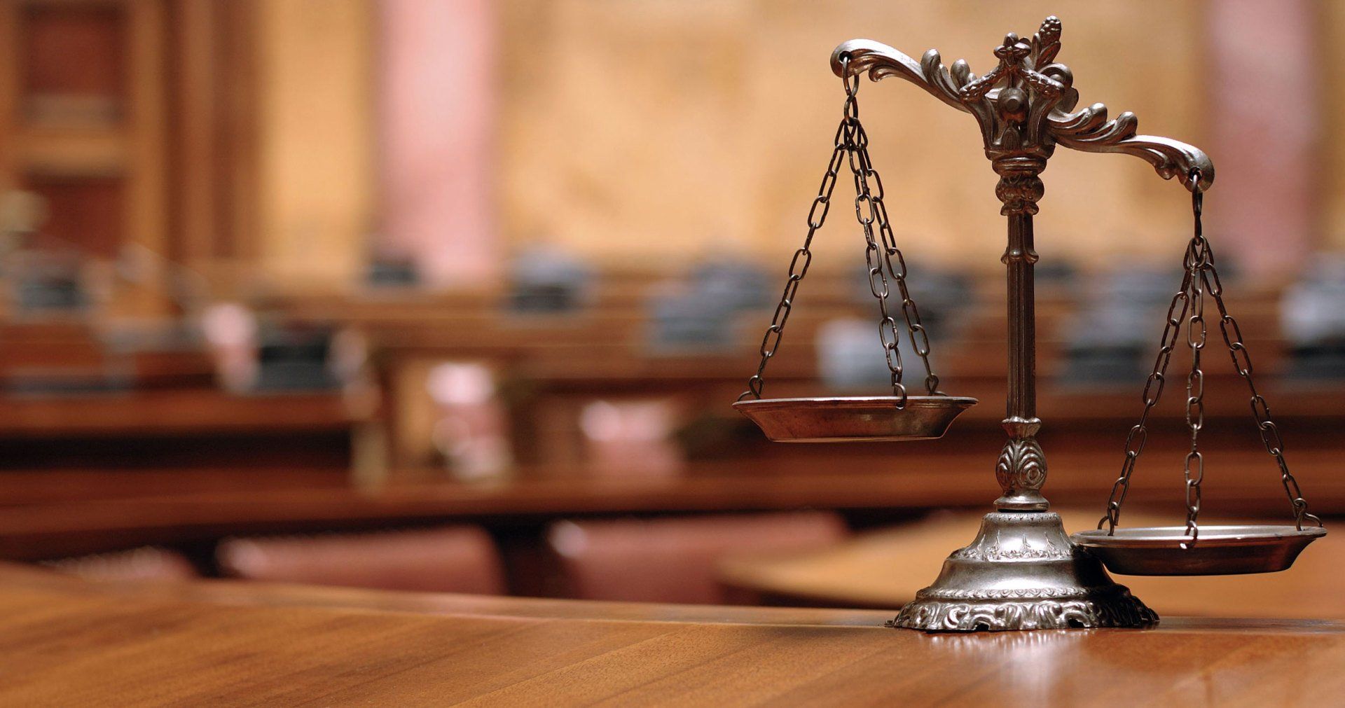 A scale of justice sits on a wooden table in a courtroom