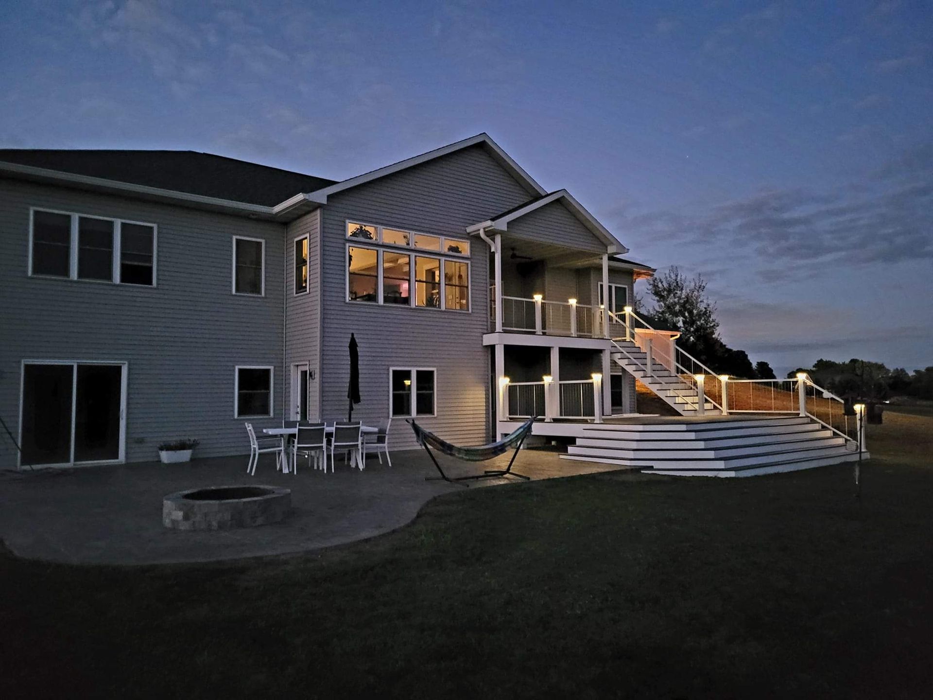 A large house with a large deck and stairs is lit up at night.