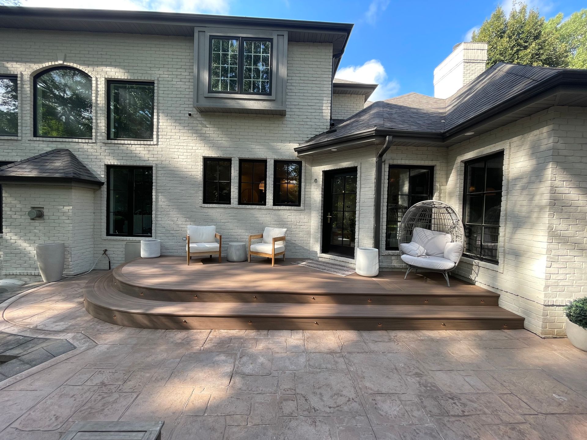 A large white brick house with a patio and chairs in front of it.