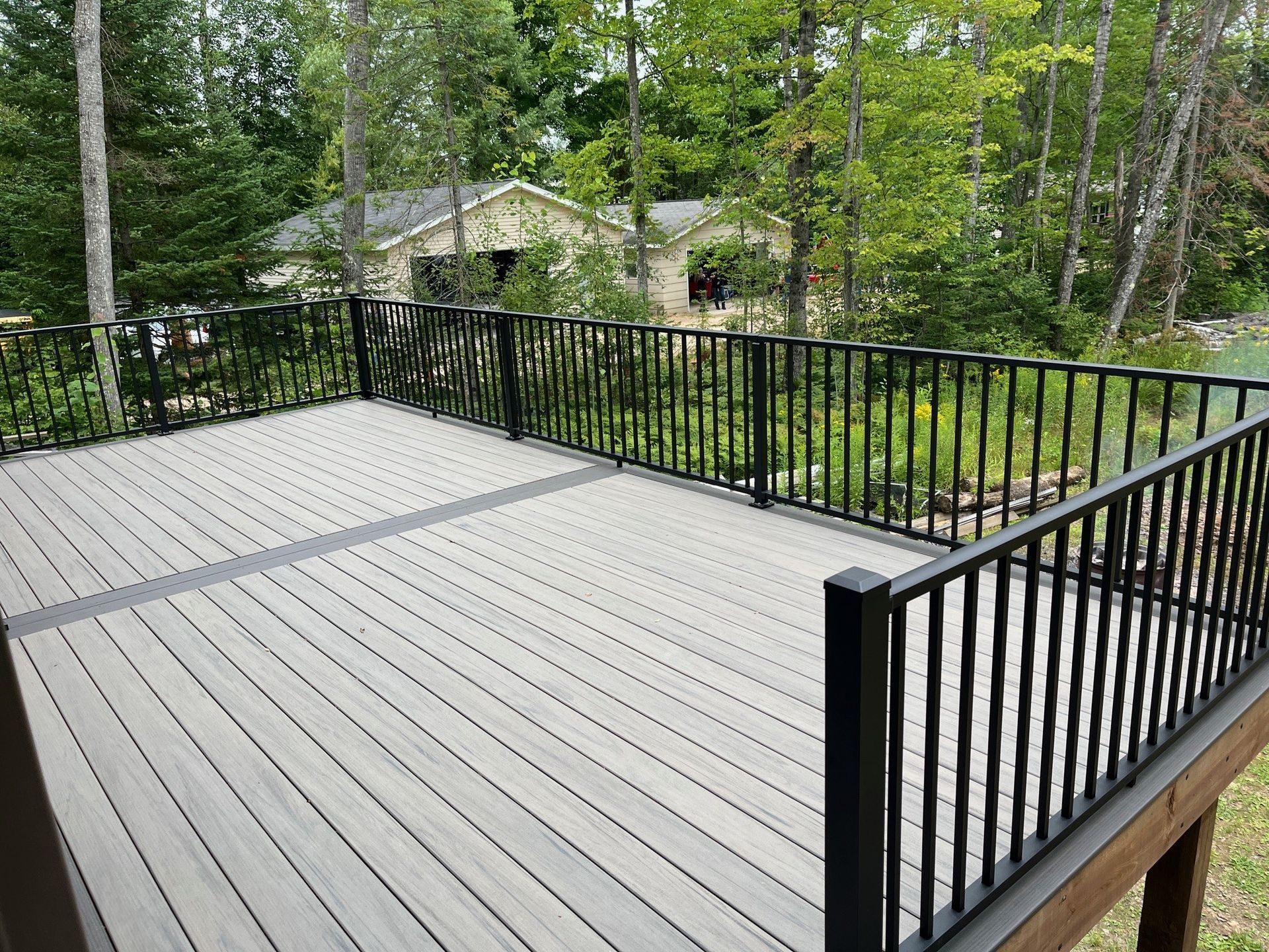 A large deck with a black railing and a house in the background.