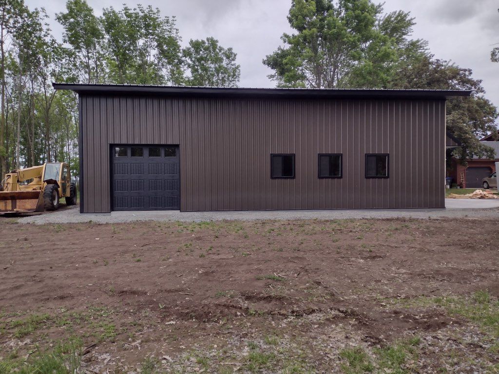 A shed with a metal exterior and a dark gray garage door on the left side