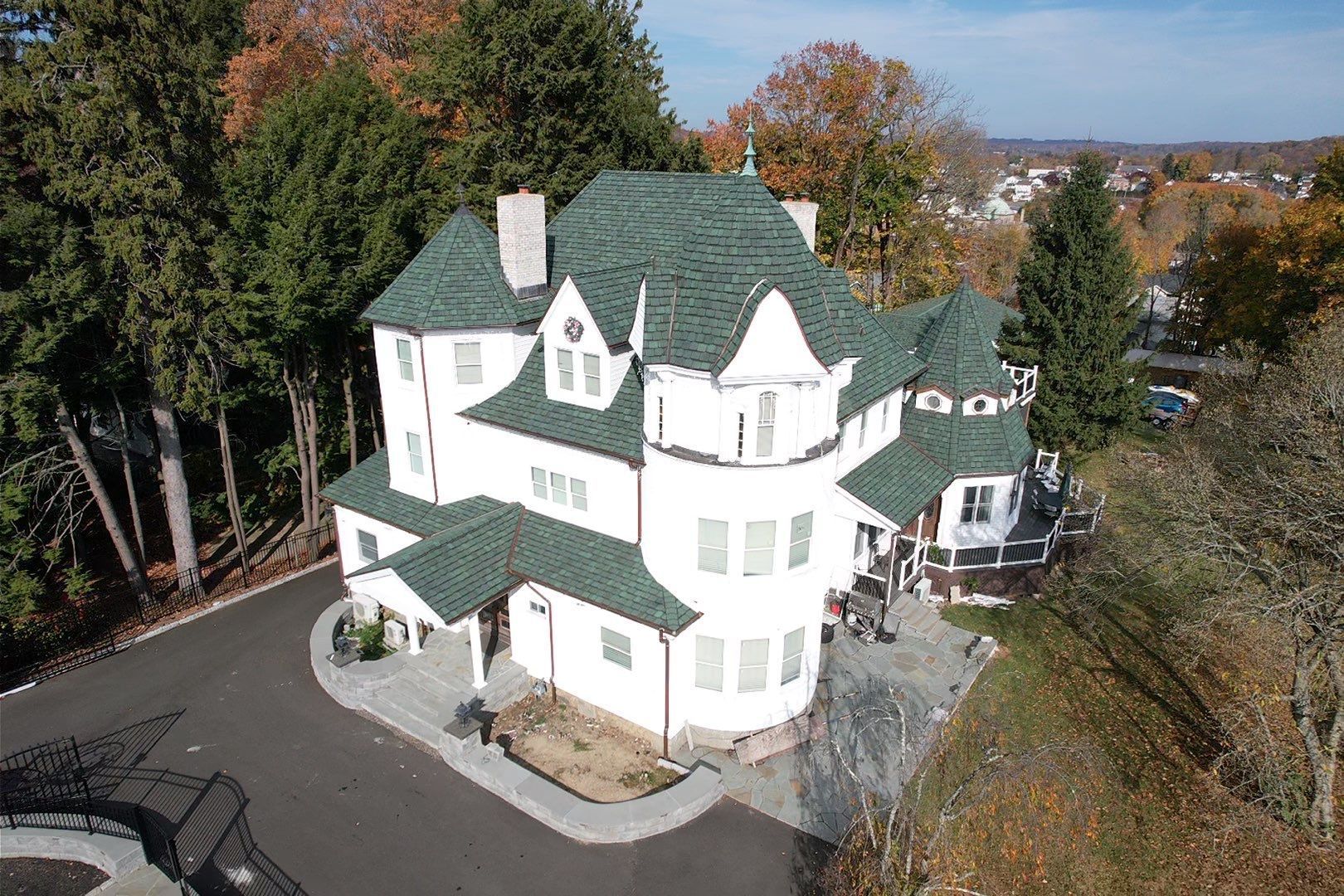 An aerial view of a large white house with a green roof surrounded by trees.