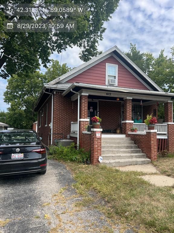 Red brick house with porch and steps, car parked in driveway, overcast day.