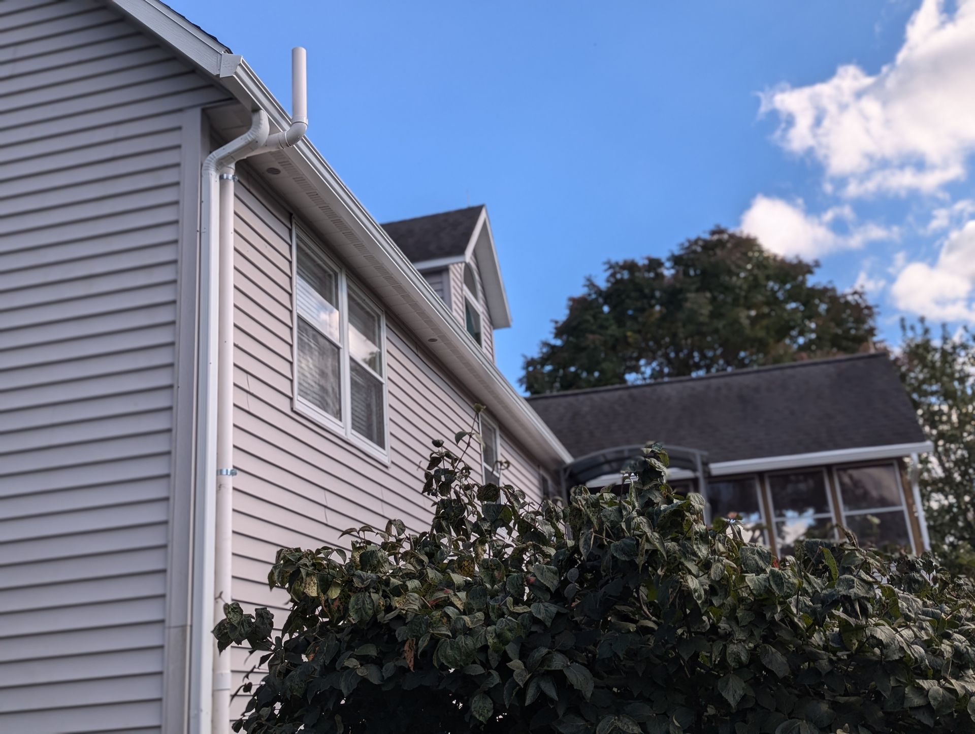 Light gray house with white trim, gutters, and a chimney against a blue sky with some clouds.