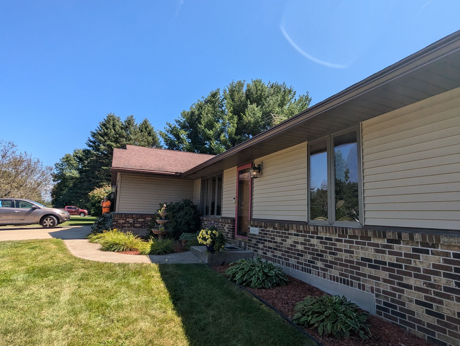 Beige house with brown roof and brick accents, blue sky, and green lawn.
