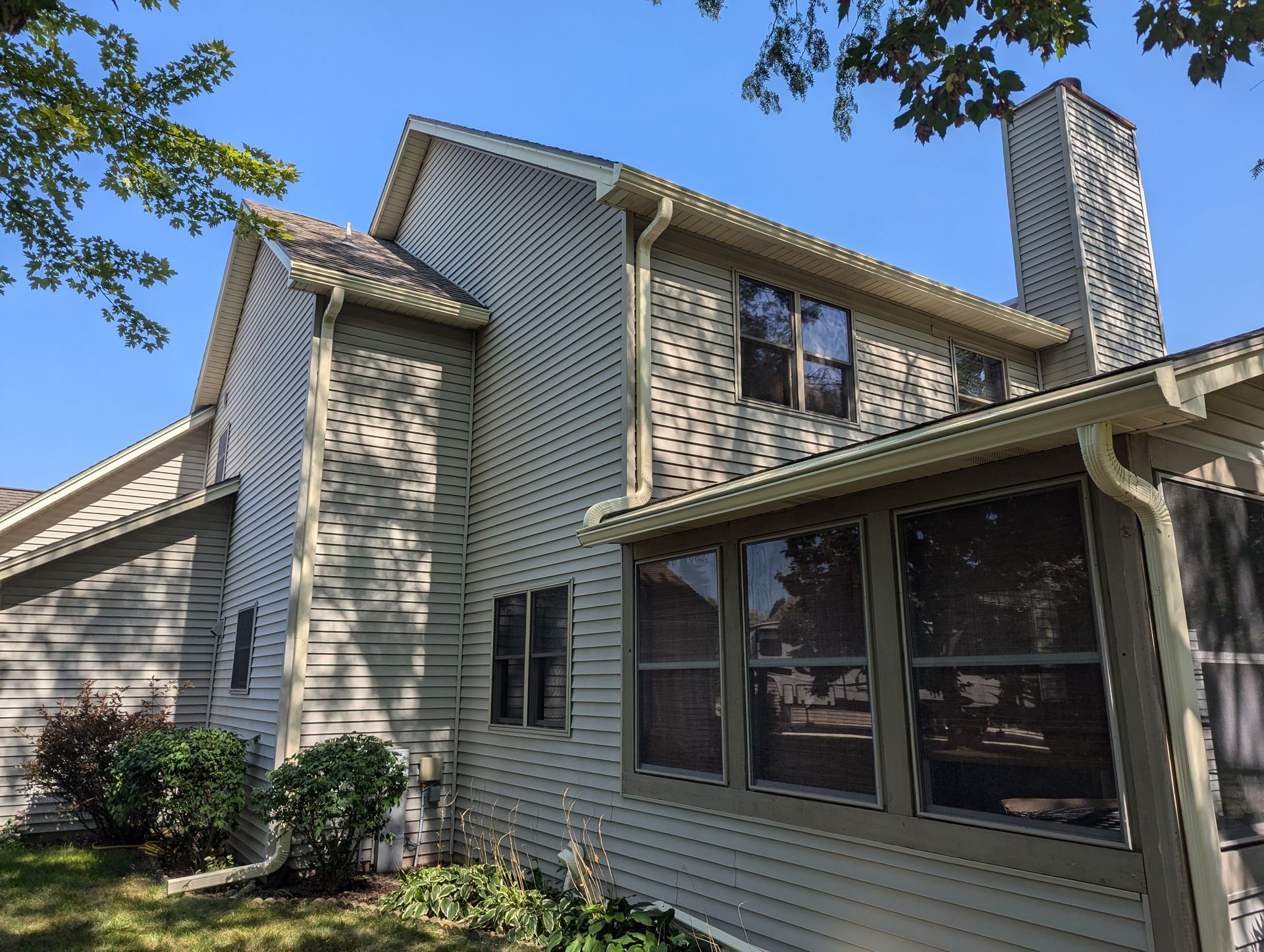 Beige two-story house with a chimney and windows, seen from a low angle on a sunny day.